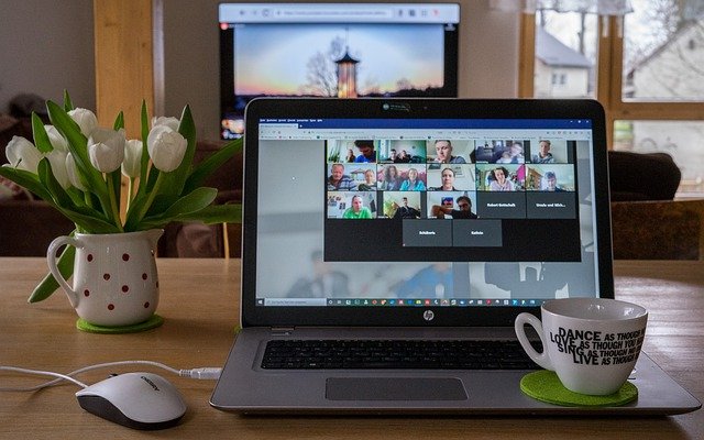 Laptop on table with flowers and coffee mug with a virtual event taking place on the screen.
